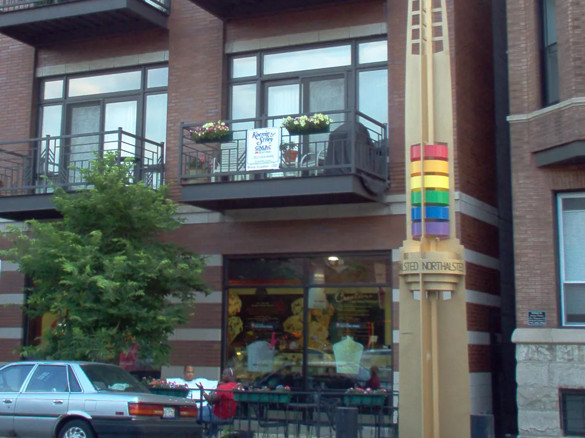 One of the rainbow pylons on Halsted Street in front of a brick condo building with balconies