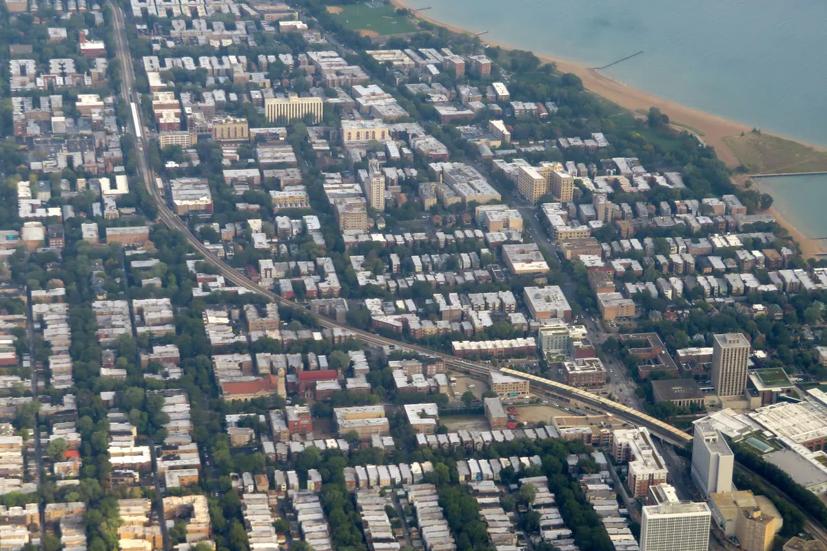 Aerial view of Rogers Park's dense blocks running to the Lake Michigan shoreline, with the elevated train line cutting through