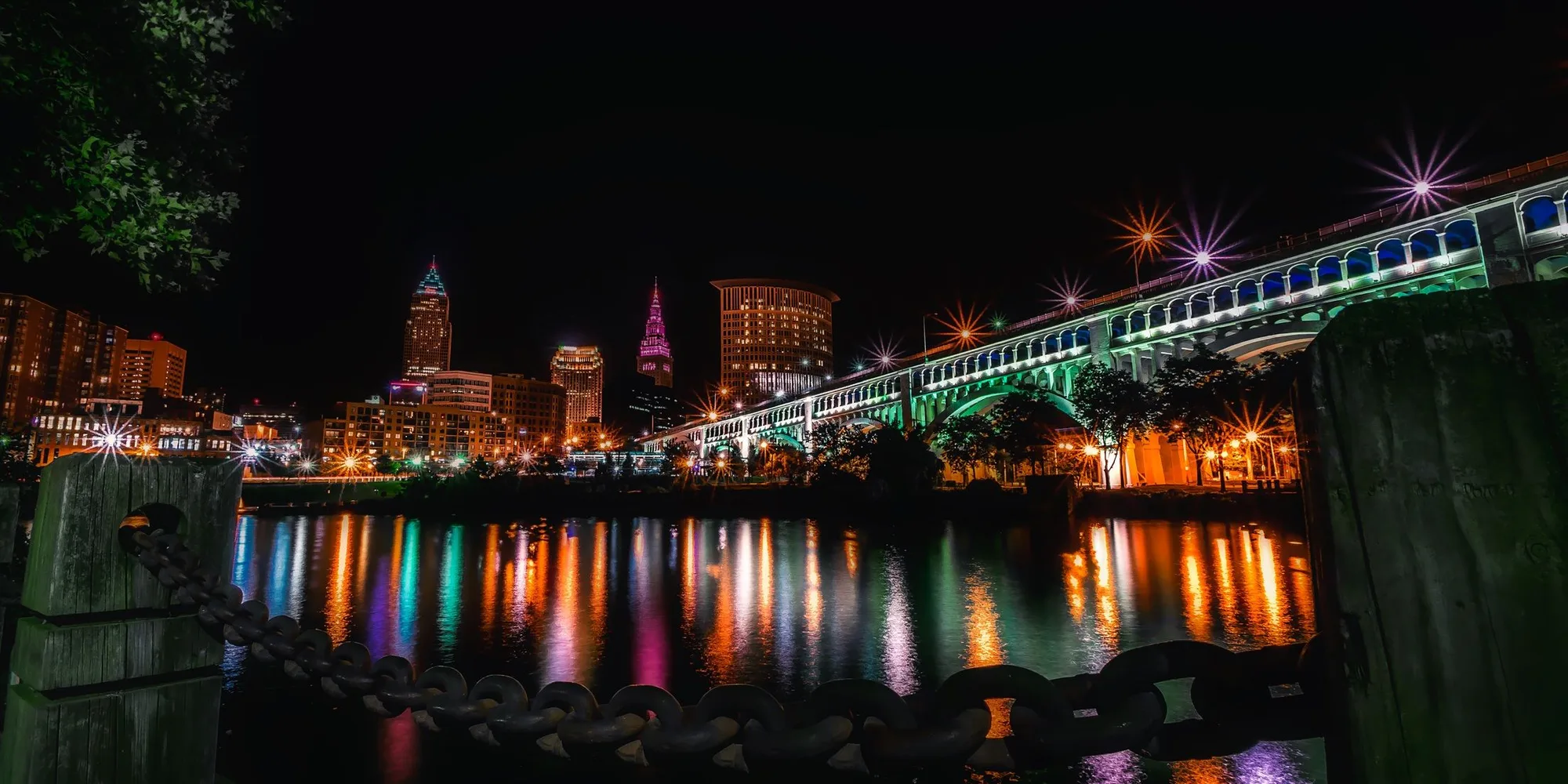The Cleveland skyline at night across the Cuyahoga River with the lit Detroit-Superior Bridge